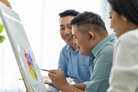 young asian man with down syndrome painting puzzle pieces with parents