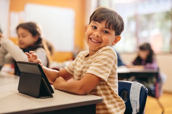 Child smiling at school while using his tablet in the classroom