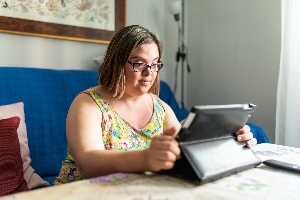 young woman with down syndrome looking at tablet on the couch